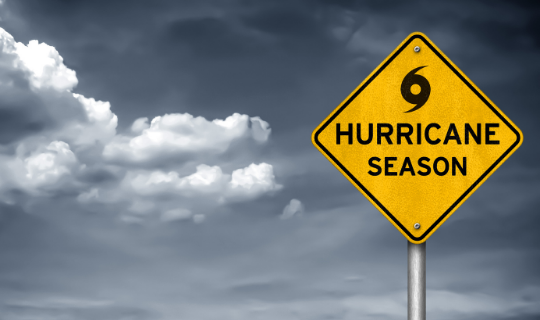 Grey clouds behind a yellow sign with a hurricane symbol and the words "hurricane season"