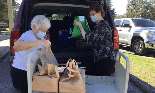 2 Volunteers loading filled bags with books into vehicle to deliver to to Homebound patrons.