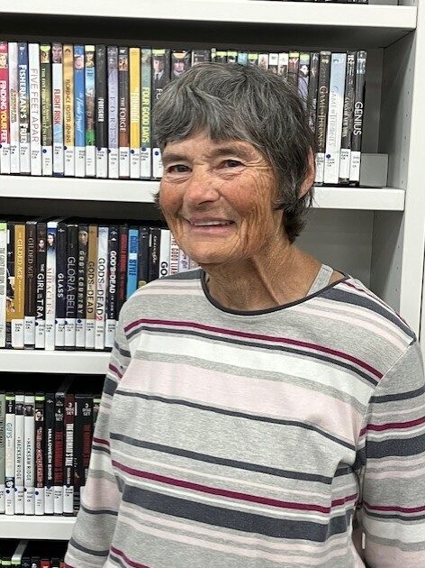 CR - Feb 2026 - Rummler Picture Volunteer Peggy, smiling and standing in front of a bookcase.