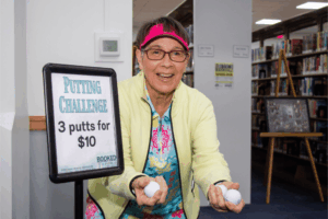 Library volunteer Joanne Tuxbury encourages attendees to participate in the new Putting Challenge. Participants were putting for the chance to win a golf foursome to a local Citrus County course.