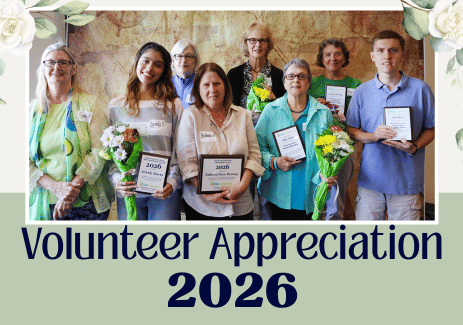 Group photo of volunteers holding award plaques with text Volunteer Appreciation 2026 on neutral green background and floral embellishments